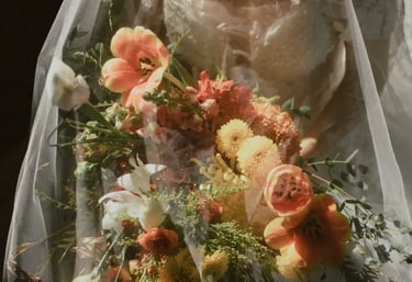 Novia con vestido de encaje bajo velo transparente sosteniendo un ramo en tonos naranja, blanco y verde.