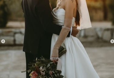Novios abrazados al atardecer con ramo en tonos rosados.