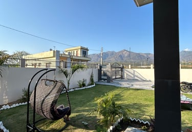 A modern garden landscape featuring a wicker hanging egg chair on a lush green lawn with mountain views.