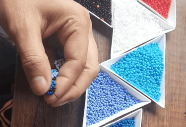 manos tejiendo una manilla con mostacillas azules