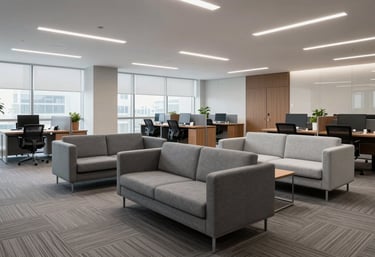 A clean and organized office lounge in a North American corporate building. Comfortable seating in slate gray and light gray fabrics with wide-angle framing showing a premium environment.