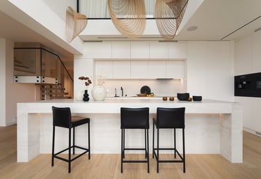 Nowoczesna biała kuchnia z dużą wyspą i ażurowymi lampami.