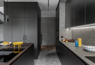 Nowoczesna ciemna kuchnia z wyspą, ściana i podłoga z szarego lastryko oraz żółte dodatki.