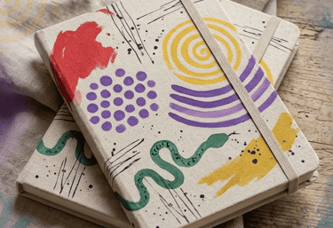 Dos diarios de tapa dura con patrones de arte abstracto y bandas elásticas sobre una superficie