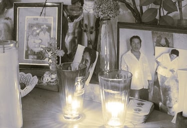 Altar conmemorativo con fotografías familiares enmarcadas, velas encendidas y símbolos religiosos