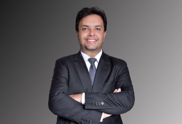 Professional corporate headshot of a smiling businessman in a black suit with arms crossed.