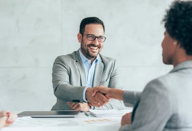 A smiling loan officer in a grey suit shaking hands during a successful loan closing.