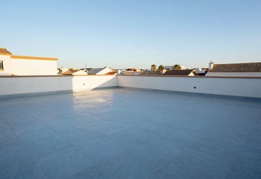 A photograph showing a finished rooftop terrace with expert waterproofing and elegant light blue floor tiles under a clear Spanish sky.