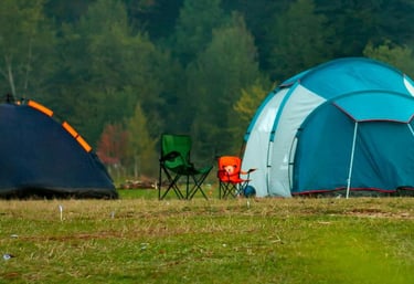 Two camping tents and foldable chairs set up on a grassy field