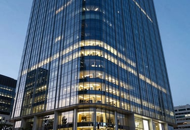 A wide architectural shot of a modern glass skyscraper in a Global / Professional financial district at dusk, glowing with Ocean Blue and Cool Off-White interior lights.
