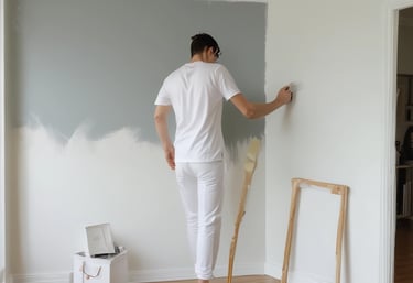 Professional house painter applying light grey paint to a white wall during a home renovation.