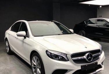 A sleek black luxury car being expertly parked by a sharply dressed valet at a grand hotel entrance.