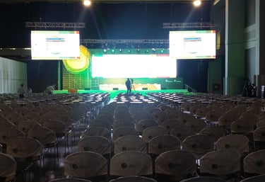 Empty conference hall with rows of chairs facing a stage with bright LED screens for a corporate event.