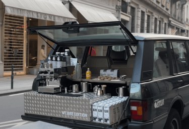 A mobile espresso bar coffee station built into the trunk of a vintage Range Rover on a city street.