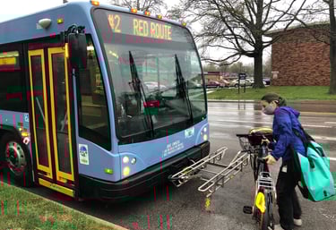Photo of a person putting their bike on the rack installed on the front of a public bus