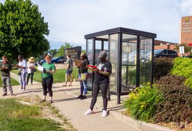 Photo of a bunch of people standing near a bus stop filling out paper surveys