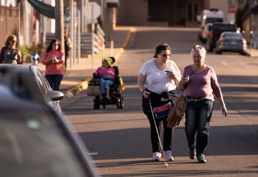 Group of people walking on the street, one in a mobility scooter, and one using a white cane