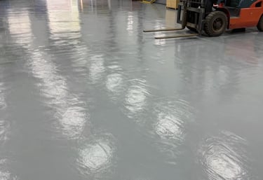 Industrial warehouse floor with sleek, metallic epoxy finish reflecting overhead lights.