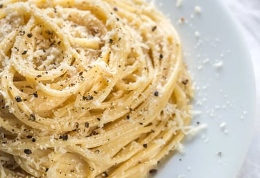 Close-up of creamy cacio e pepe pasta sprinkled with Pecorino Romano cheese and cracked black pepper