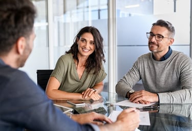 A smiling couple meeting with a professional financial advisor in a modern office to discuss business planning.