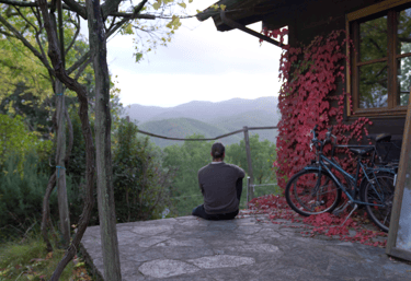 a man sitting on a stone patio with a bicycle in documentary scene