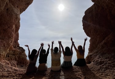 Five friends raising their arms inside a sea cave overlooking the bright sun and ocean in Algarve.
