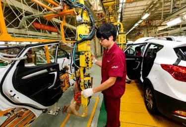 Operário em fábrica de carros na China trabalhando na linha de montagem automatizada com veículos em