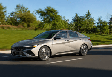 Hyundai Elantra 2026 prata em movimento em rodovia com paisagem arborizada ao fundo.