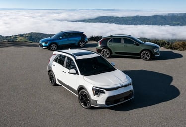 Três versões do Kia Niro híbrido estacionadas em mirante com vista para montanhas e nuvens.