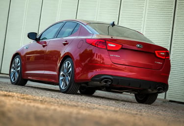 Kia Optima vermelho visto de traseira em estacionamento, sem placa traseira visível.