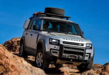 Land Rover Defender prata enfrentando trilha rochosa em cenário off-road com céu azul ao fundo