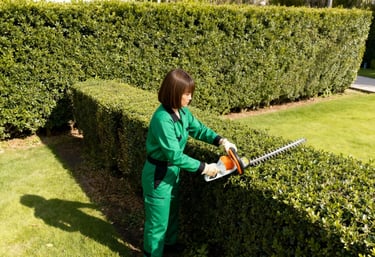 a woman in green workwear is using a hedge trimer