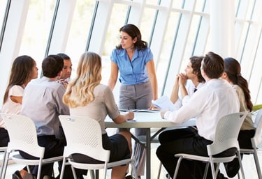 photo d'une femme debout parlant à une équipe assise à une table autour d'elle