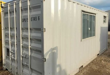 container para obra na cor cinza com uma janela em uma paisagem no patio de um estacionamento