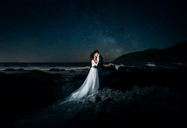 a bride and groom standing on a rocky beach under a starry sky