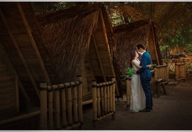a bride and groom standing in front of bamboo huts