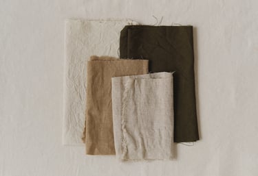 Neutral folded linens stacked on fabric, symbolizing simplified belongings and gentle decluttering.