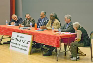 A panel of speakers sit at a table with a sign saying we support peace with justice for palestinians