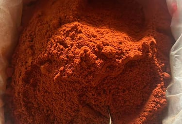 Close-up of vibrant red chili powder inside a large bag with a metal measuring scoop.