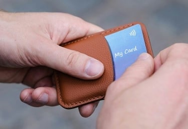 2 hands pulling a digital business card out of a stylish leather card holder on a blurry grey cloud background