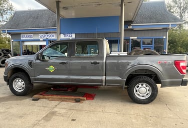 A gray Ford F-150 truck lifted on a red hydraulic jack at an automotive tire and brake service shop.