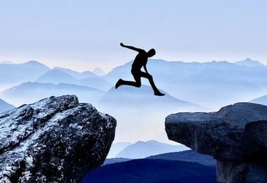 a man jumping over a cliff with a mountain in the background