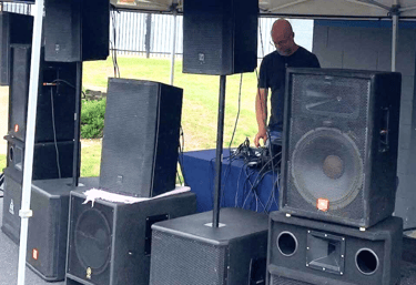 man outdoors under a tent standing behind speakers