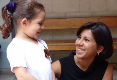 A teacher hunkers down to talk with a student. Both the teacher and the student are smiling.