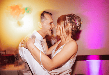 Les mariés dansent et sourient sous les lumières colorées pendant la soirée.
