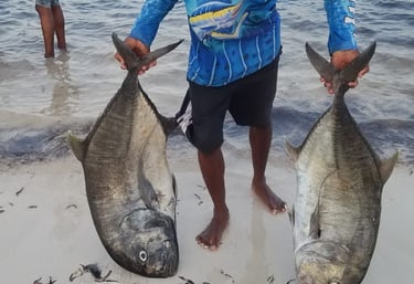 a man holding two fish on the beach