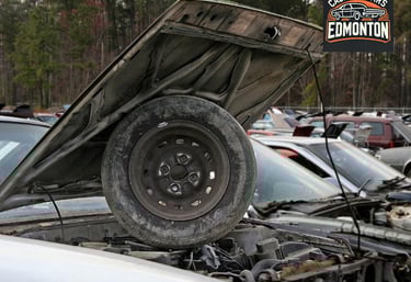 A scrap car with a hood up parked in a junk yard.