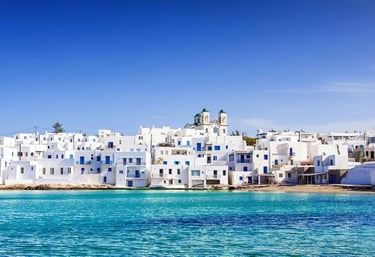 Scenic view of white houses and blue windows in Naoussa, Paros island, overlooking turquoise Aegean Sea water.