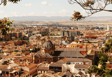 Panoramic cityscape view of Granada, Spain, featuring red-tiled roofs and the historic church of San Jeronimo.