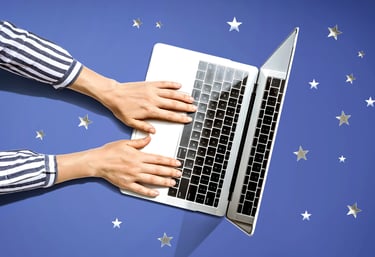 Hands typing on a laptop that is sitting on a blue surface covered in silvery stars.